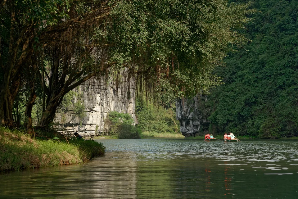 Rowing boats with visitors in orange life vests on the river below limestone cliffs at Trang An, Ninh Binh