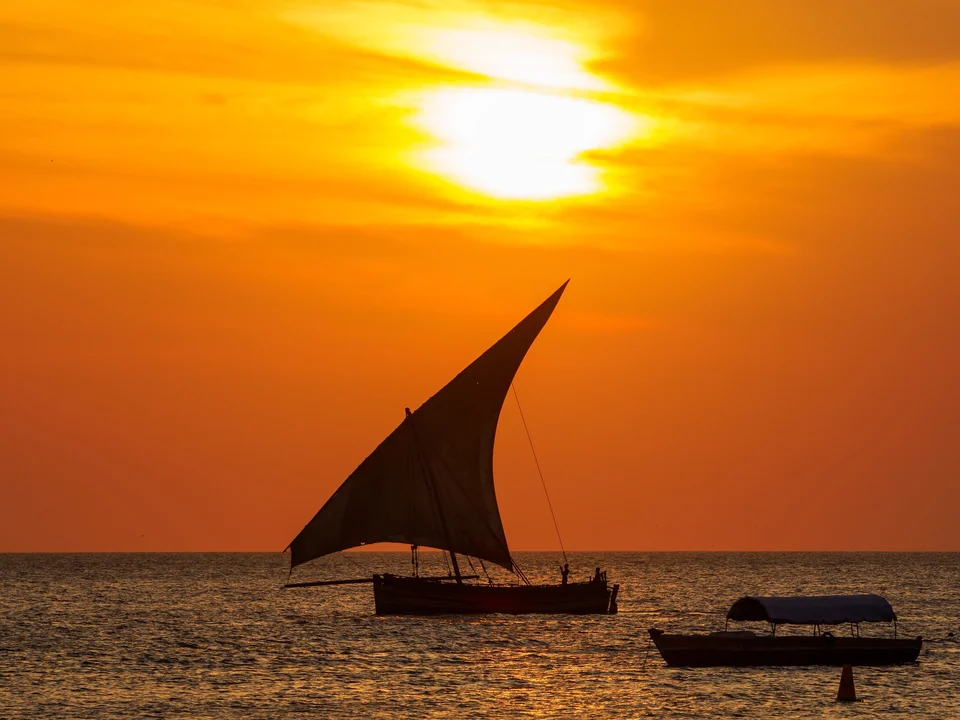 Traditional wooden sailing boat crossing the sunset sky off the harbor of Stone Town, Zanzibar